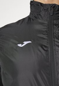 Black zip-up jacket made of lightweight material. Features a high collar and a small embroidered logo on the left chest.