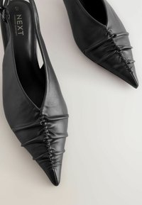 Schwarze Leder-Slingbacks mit spitzem Zehenbereich und gerafften Details an den Seiten. Mit offener Ferse und Knöchelriemen.