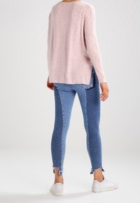 Světle růžový pletený svetr s dlouhými rukávy, doplněný modrými skinny džíny s roztrženými lemy a bílými teniskami.