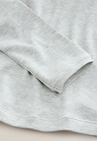 Detalle de manga y dobladillo de camisa de manga larga acanalada en gris claro, mostrando la textura y las costuras en tela suave.