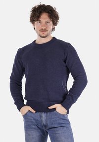 Maglione lavorato a maglia blu navy con collo rotondo, polsini e orlo a coste. Indossato sopra jeans azzurri, il tessuto testurizzato aggiunge profondità. Vestibilità casual.