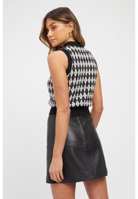 Knitted black and white argyle sleeveless top with a black ribbed waist, paired with a black leather mini skirt featuring stitched paneling.
