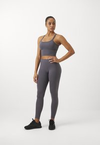 Gray athletic crop top and high-waisted leggings, made of smooth, stretchy material. Model wears black athletic shoes.