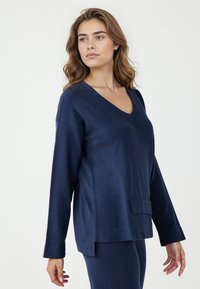 Maglione blu navy a scollatura a V con maniche lunghe, texture morbida e tasca a toppa frontale; presenta spacchi laterali e un design comodo.