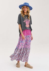 Šedé zkrácené tričko s růžovou grafikou, vrstvené přes dlouhou barevnou maxi sukni s paisley vzory, doplněné béžovými balerínami.