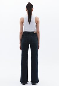 Džíny s vysokým pasem, tmavě modré, s rozšířenými nohavicemi a hladkým povrchem, se dvěma zadními kapsami a koženou nášivkou s logem na pase.