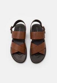 Braune Ledersandalen mit Kreuzriemen-Design, verstellbarem Schnallenverschluss und dunkler Gummisohle. Glatte Textur und minimalistischer Stil.