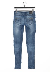 Jeans ajustados azules hechos de mezclilla con un lavado desgastado, diseño de cinco bolsillos y costuras visibles en los bolsillos traseros. Cuelga de un clip negro.