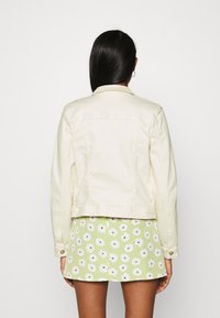 Ljus denimjacka med klassisk design, som har en spetsig krage, knappade ärmmuddar och sömnadsdetaljer, i kombination med en blommig kjol.