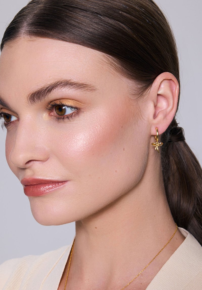 Złota kolczyk w kształcie koła z kwiatowym wzorem, o polerowanym wykończeniu. Odcień skóry wygląda naturalnie z minimalnym makijażem, a włosy są gładkie.