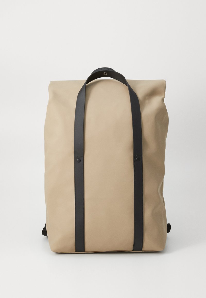 Roll-top backpack in beige fabric, featuring black leather straps, a smooth texture, and subtle hardware accents. Minimalist design.