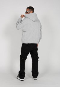Hanorac gri cu glugă, cu o croială lejeră, asortat cu pantaloni cargo negri cu buzunare laterale și accesorii metalice argintii, purtat cu ochelari de soare negri.