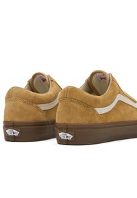 Semišové tenisky v hořčicově žluté barvě s bílými pruhy, polstrovaným límcem a hnědou gumovou podrážkou. Na patě je logo.