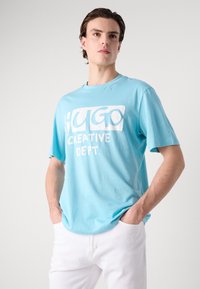 Lys blå bomulls T-skjorte med en dristig hvit grafisk trykk som sier "HUGO CREATIVE DEPT." Rund hals og korte ermer.