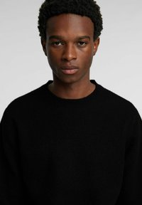 Klassischer schwarzer Pullover mit rundem Ausschnitt, gefertigt aus einem weichen, strukturierten Stoff. Verfügt über eine lockere Passform und gerippte Bündchen.