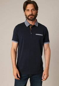 Polo shirt marine avec un col à motifs, une patte de boutonnage à trois boutons et une poche poitrine. Manches courtes avec des détails contrastants. Tissu en mélange de coton.