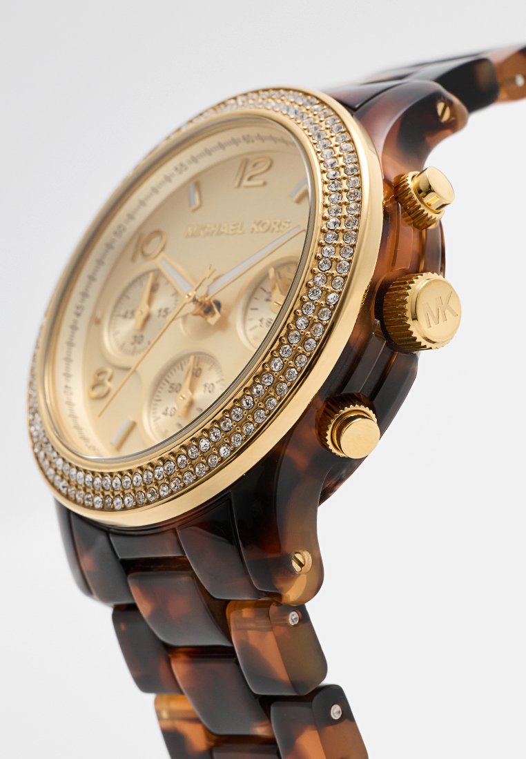 Montre chronographe dorée avec un cadran beige, des index horaires ton sur ton, des accents en cristal et un bracelet en écaille de tortue. Comprend trois sous-cadrans.