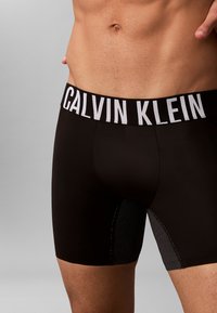 Calzoncillos bóxer negros con un logo blanco de Calvin Klein en la cintura, con un diseño ajustado y paneles laterales texturizados para mayor transpirabilidad.