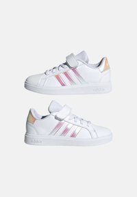 Vita sneakers med tre iriserande ränder, en vadderad tunga och ett kardborreband. Texturerad gummiklös och slät syntetisk ovandel.