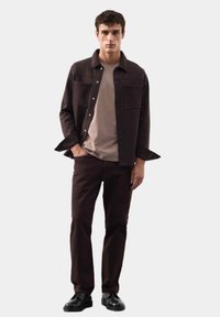 Ciemnobrązowa kurtka zapinana na guziki z dwoma przednimi kieszeniami, w połączeniu z jasno-brązowym t-shirtem i dopasowanymi ciemnobrązowymi spodniami. Czarnę buty dopełniają całość.