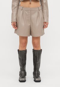 Beige faux leather shorts with pleats, featuring a flat waistband. Paired with knee-high, dark gray leather boots with buckled straps.