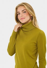 Olive zelen zgornji pulover s turtleneck ovratnikom, z rebrastimi manšetami in ovratnikom, izdelan iz gladkega materiala, prilegajoče zasnove, ki ima dolge rokave in zaobljen rob.