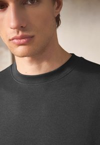Czarny sweter z prążkowanej dzianiny z okrągłym dekoltem, o gładkiej fakturze i minimalistycznym designie. Zbliżenie, podkreślające szczegóły tkaniny.