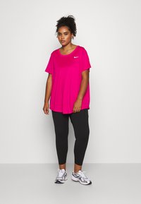 Fuchsia træningstrøje med korteærmer og rund hals, kombineret med sorte leggings og sølvfarvede træningssko. Nike-logo synligt.