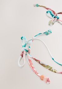 Dva barvita tkaninska vozla s cvetličnimi vzorci v roza, modro-zeleni in beli barvi, z okrasnimi kroglicami na koncih. Mehka tekstura in prilagodljiva oblika.