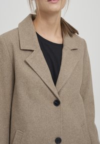 Cappotto in misto lana beige con colletto a revers, design a un solo petto e bottoni neri. Presenta due tasche laterali e una texture liscia.
