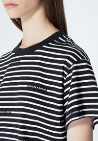 Svart och vitrandig t-shirt med korta ärmar och rund halsringning, med en logotryck "KOOPLES X SPORT" längs ränderna.