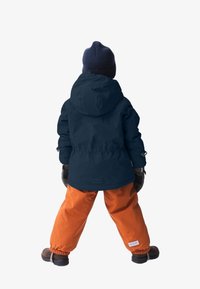 Wasserabweisende marineblaue Jacke mit Kapuze und elastischen Bündchen, kombiniert mit leuchtend orangefarbenen Hosen. Enthält Handschuhe und robuste braune Stiefel.