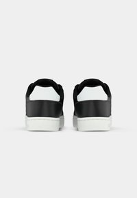 Un paio di sneaker basse bianche e nere viste dal retro, isolate su uno sfondo chiaro con suole bianche.