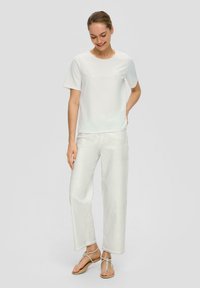T-shirt blanc à manches courtes avec un col rond, associé à un jean blanc léger et ample. Les sandales présentent des lanières minimalistes.