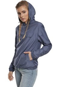 Giacca leggera con cappuccio di un profondo blu navy, dotata di una tasca frontale, polsini elasticizzati e cordino sul cappuccio. Tessuto liscio e resistente all'acqua.