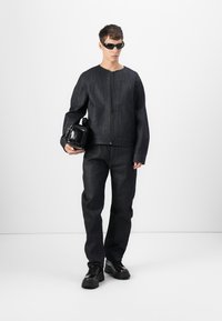 Dark denim jacket with a high neckline and front zipper, paired with matching loose-fitting pants. Accessory: small black handbag. Black sunglasses.