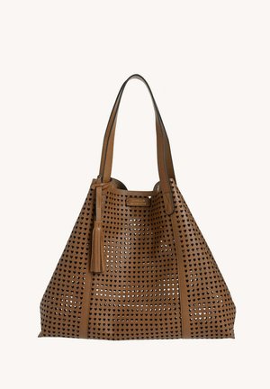 Sac fourre-tout en cuir marron avec des perforations en forme de cœur, des doubles bretelles et un gland décoratif suspendu à une bretelle.