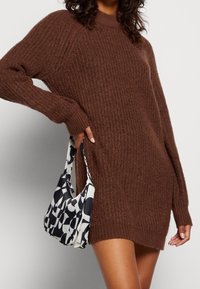 Pull en maille côtelée marron à manches longues, accompagné d'un sac à main noir et blanc à motif, de forme arrondie avec une anse courte.