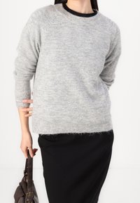 Vaaleanharmaa neulottu paita pyöreällä pääntiellä, resorit hihansuissa ja helmassa. Yhdistetty mustaan hameeseen ja tummanruskeaan käsilaukkuun.