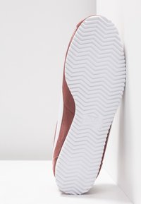 Semelle d'une basket Nike bordeaux et blanche montrant un motif de bande de roulement en zigzag blanc et un logo Nike en relief discret.