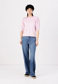 Light pink short-sleeve top with puffed sleeves, paired with flared blue denim jeans and black flat shoes. Hat is black with a rounded shape.