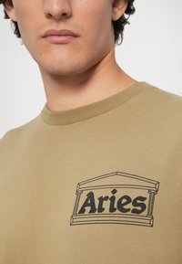 Olijfgroene sweatshirt met een zwarte grafiek waarop het woord "Ram" staat afgebeeld binnen een decoratief architecturaal kader. Zachte katoenmaterialen.