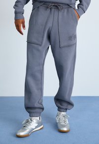Szare dresowe spodnie o luźnym kroju, z dwiema dużymi kieszeniami naszytymi i ściągaczami na nogawkach. W połączeniu z srebrnymi butami sportowymi.
