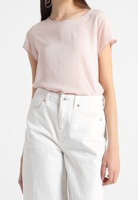 Ljusrosa kortärmad blus i kombination med högmidjade vita denimjeans, med en slät textur och en enkel rund halsringning.