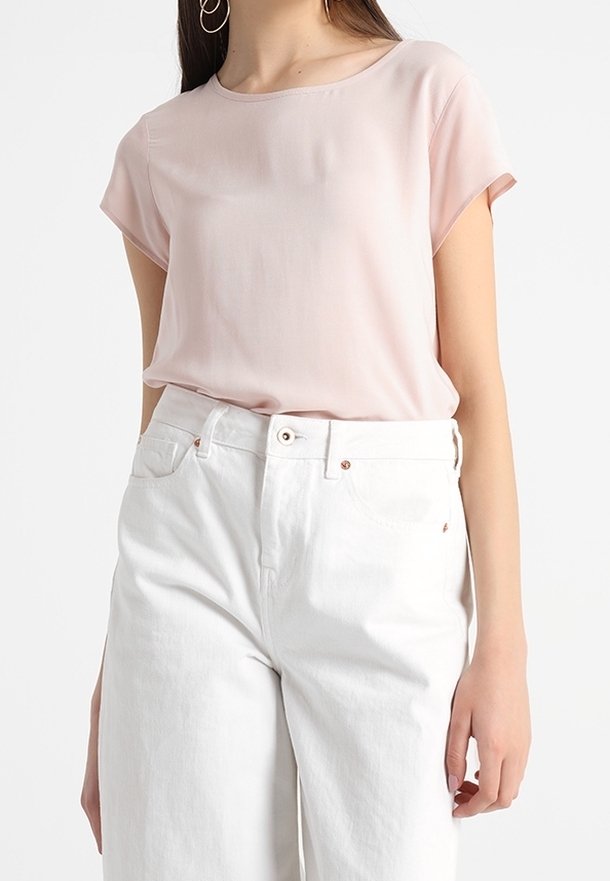 Ljusrosa kortärmad blus i kombination med högmidjade vita denimjeans, med en slät textur och en enkel rund halsringning.