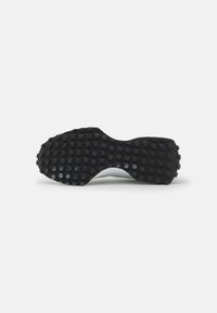 Sole of a shoe featuring a textured black rubber material with circular grip patterns, curved shape, and slight tapering towards the center.