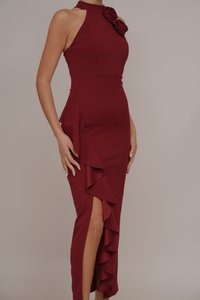 Burgundy halter neck dress with a floral accent, featuring side ruffles and a thigh-high slit, made from a stretchy fabric.