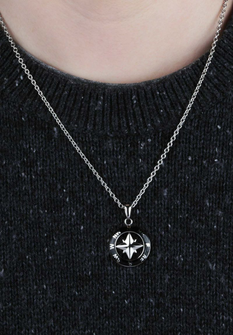 Collana in argento con ciondolo rotondo a forma di bussola nera con una stella cardinale bianca, esposta su un maglione scuro e strutturato.