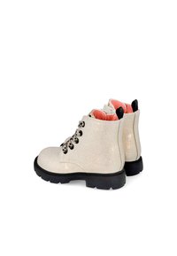 Botas de tobillo blancas brillantes con cordones negros, parte superior texturizada, forro rosa en contraste y suela de goma con un patrón de tracción.