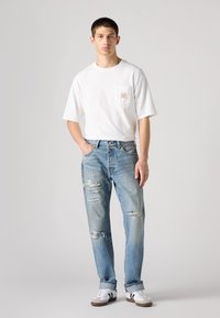 Witte T-shirt met korte mouwen en zak, versleten lichtblauwe jeans en witte sneakers met zwarte strepen. Casual, comfortabele pasvorm en gematigde slijtage.